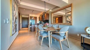 A modern dining area with a wooden table and chairs, a kitchen in the background, and a large mirror on the wall. - Luxury 2BR Condo in Nuevo Vallarta - Rooftop Pool (Nuevo Nayarit)