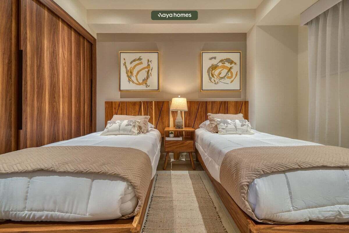 Une chambre d’hôtel avec deux lits, une tête de lit en bois, une table de chevet avec une lampe et deux œuvres d’art encadrées accrochées au mur.