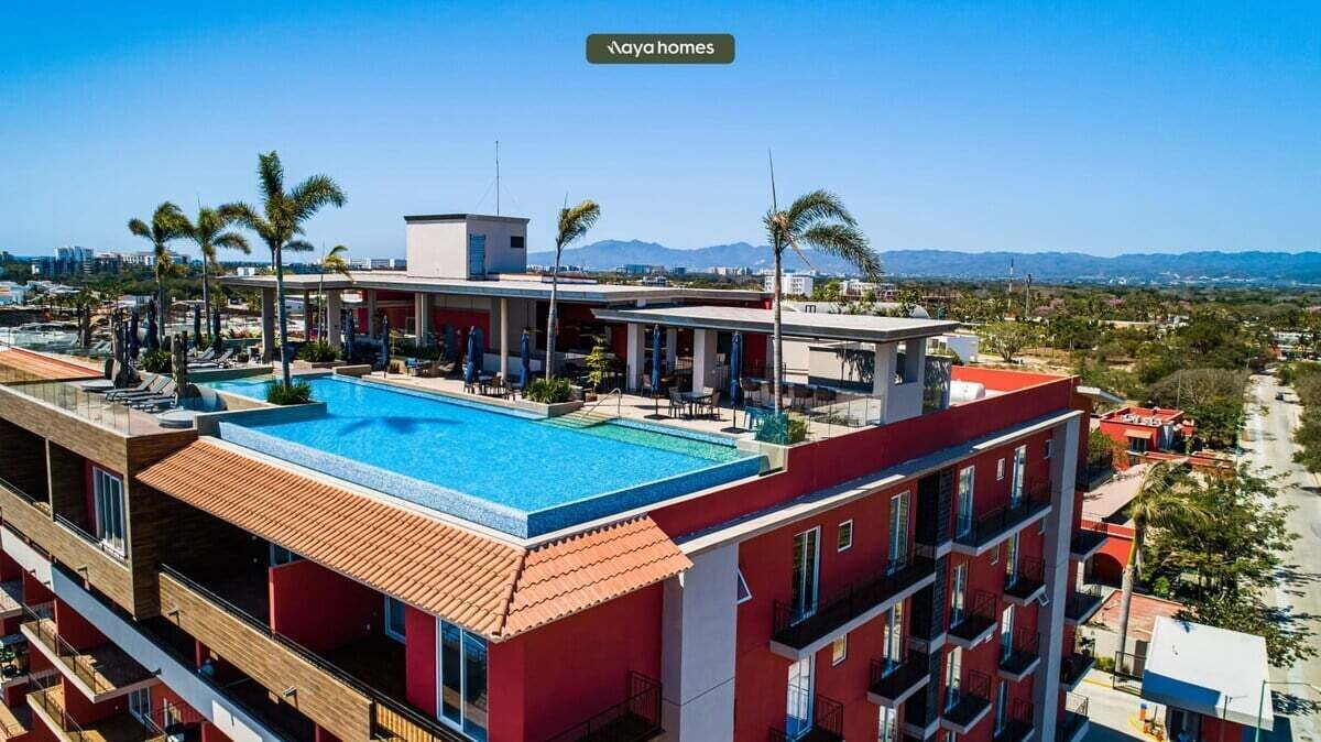 A hotel with a rooftop pool, multiple balconies, and a view of the surrounding landscape.