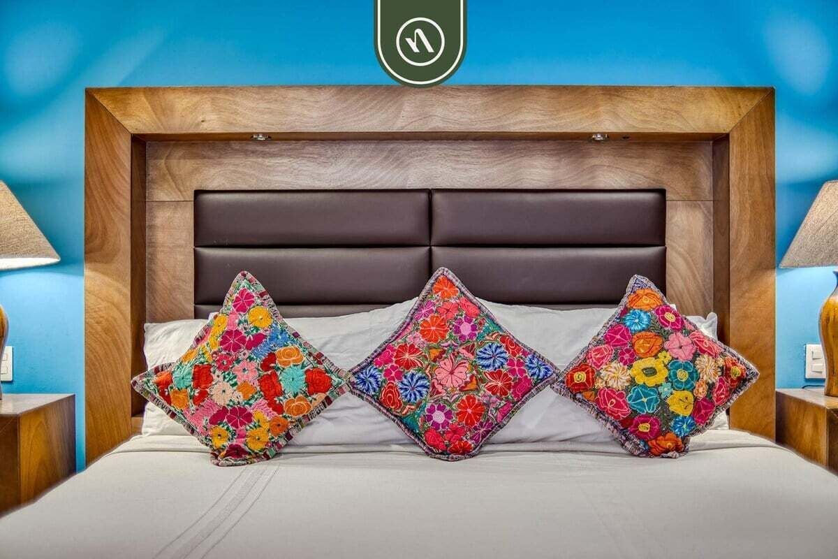 Ein Bett mit einem Holz-Kopfbrett, drei farbenfrohe Blütenkissen und zwei Nachttischlampen.