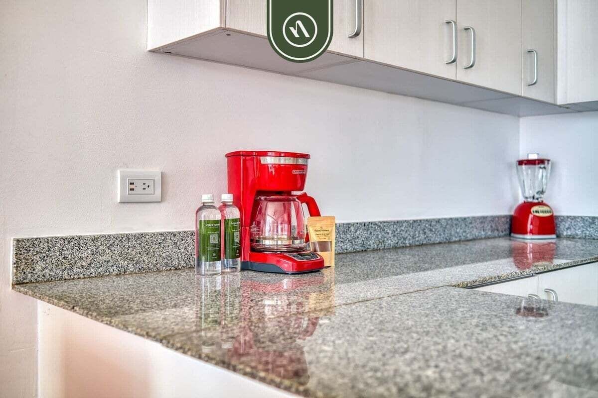 Una encimera de cocina con una cafetera roja, una licuadora y dos botellas de agua.