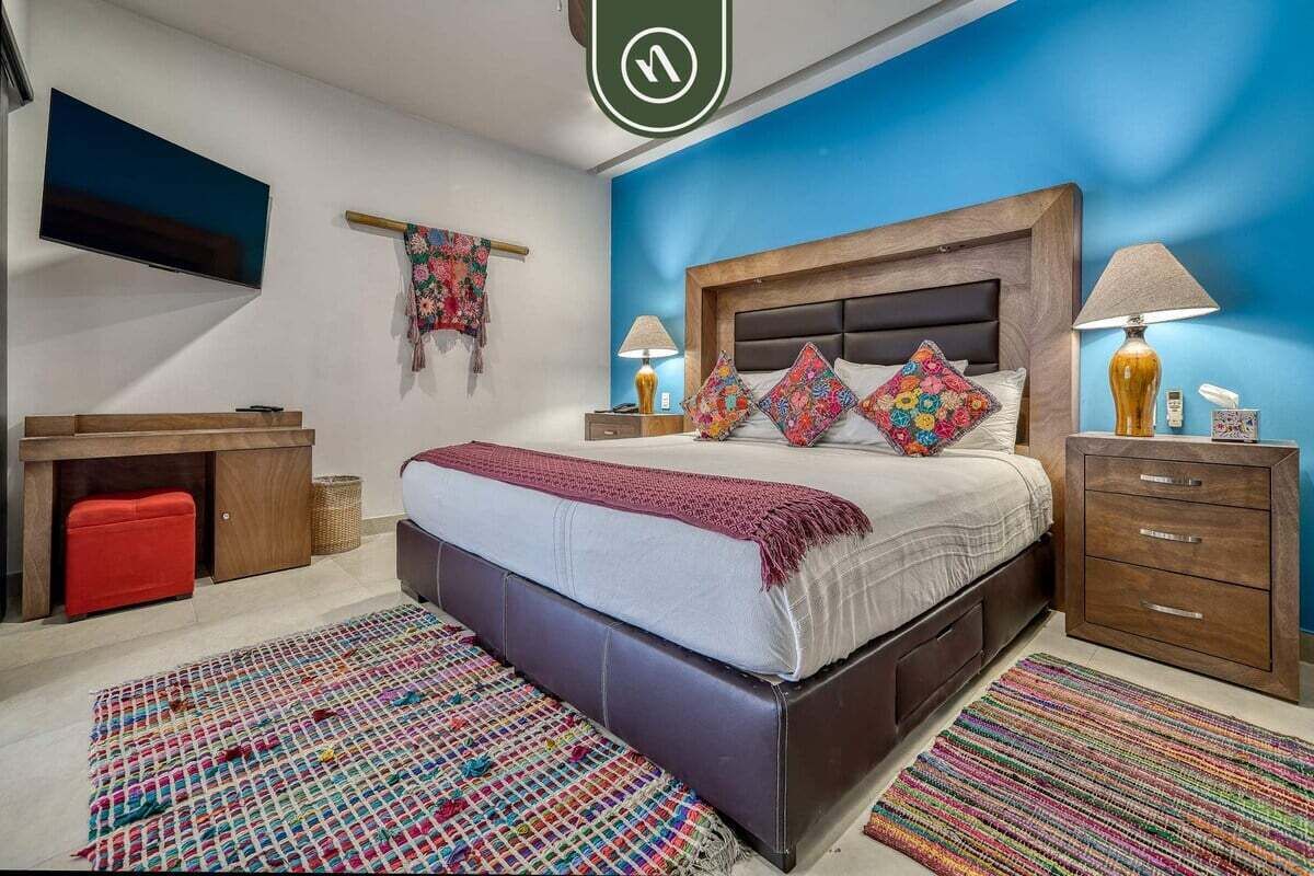 A bedroom with a bed, bedside tables, a TV, and a desk.