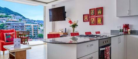 Una cocina moderna con una isla central, armarios blancos y un amplio ventanal con vistas a la ciudad.