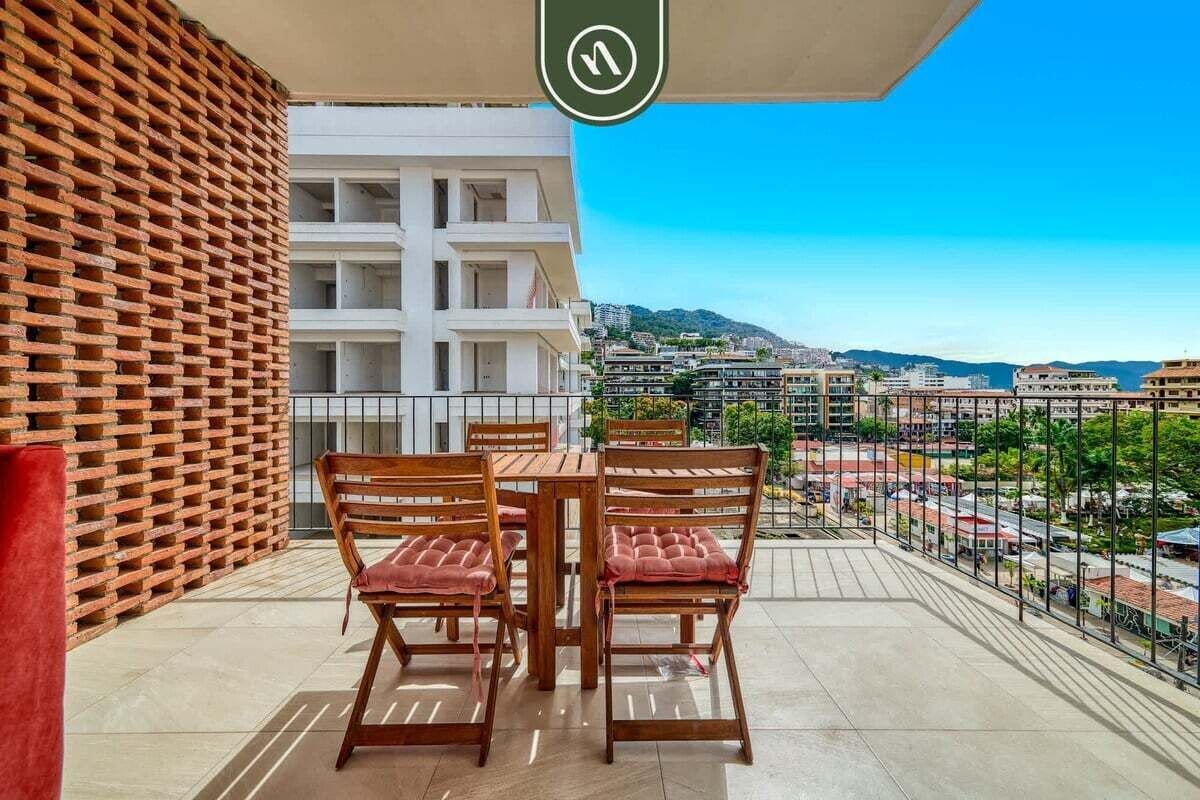 Un balcon avec une table et des chaises, une vue sur les immeubles et un ciel dégagé.