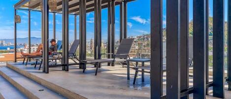 Un salón en la azotea con vistas despejadas del paisaje urbano, que cuenta con una estructura metálica moderna y sillones de descanso.