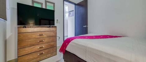 Une chambre avec une commode en bois, un lit recouvert d’une couverture rose et une porte sur laquelle est apposée une pancarte.