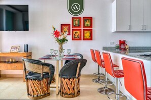 Una cocina moderna con comedor, que incluye un televisor, obras de arte y una cafetera.