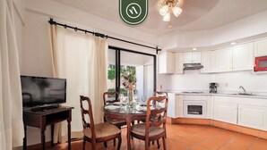 A dining area with a round table, chairs, a television, and a kitchen with white cabinets and a red microwave. - Amazing 1 BR Condo - Terrace - Pool - Romantic Zone (Puerto Vallarta)