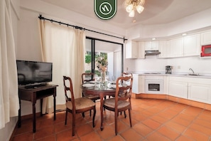 A dining area with a TV, dining table, chairs, and a kitchen with white cabinets and a red microwave.