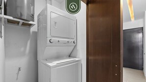 A laundry room with a white washer and dryer, a wooden door, and a metal vent. - Beautiful 2 BR Condo Amazing Rooftop Pool - Gym (Puerto Vallarta)