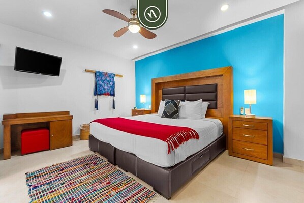 A bedroom with a bed, a TV, a ceiling fan, a nightstand, and a desk.