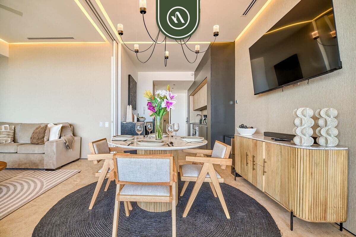 A modern living room with a round dining table, a sofa, a TV mounted on the wall, and a wooden cabinet.