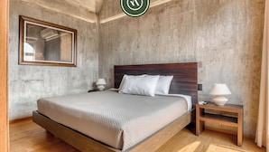 Une chambre à coucher avec un lit en bois, deux tables de chevet avec des lampes, un miroir encadré et un mur en béton.