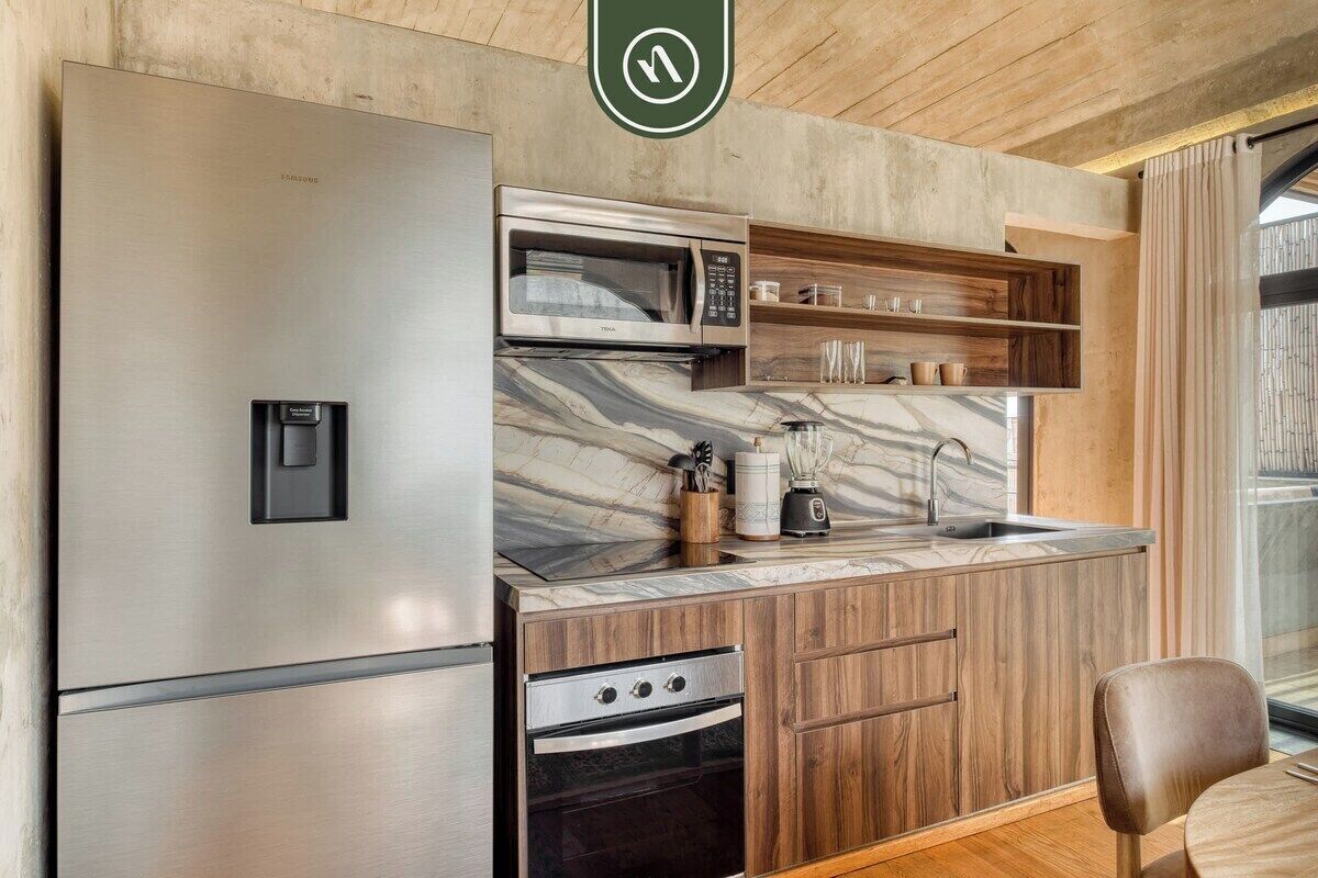 A compact kitchen with a stainless steel refrigerator, a microwave, a built-in oven, and a marble countertop.