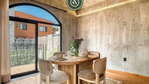 Un coin repas avec une table ronde, quatre chaises, un vase de fleurs et une vue sur un bâtiment, visible à travers une grande porte vitrée.