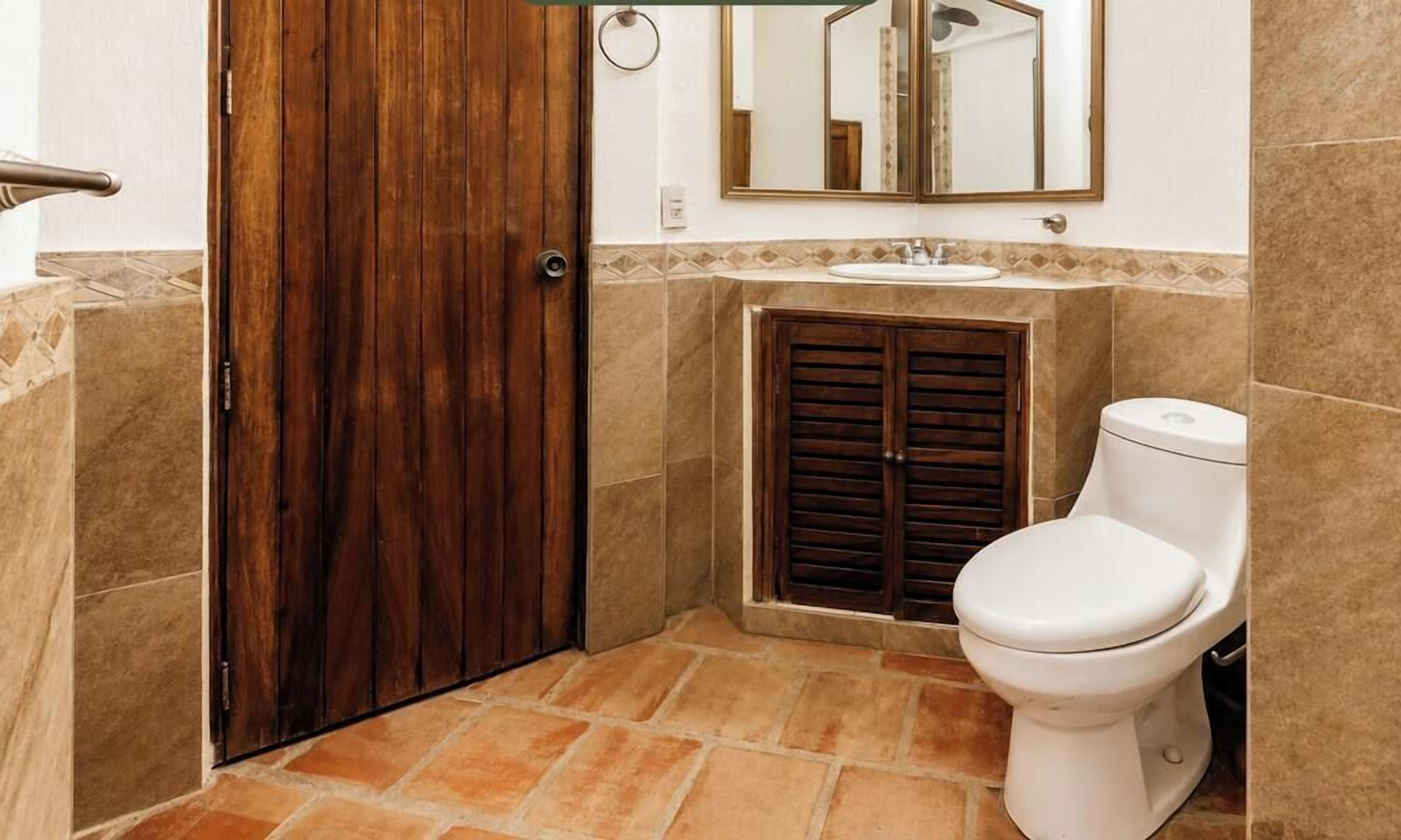 A bathroom with a wooden door, a toilet, a sink, and a mirror.