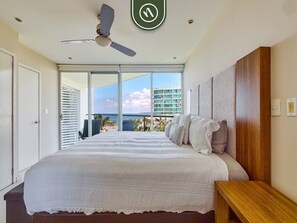 A bedroom with a large bed, a ceiling fan, a view of the ocean, and a balcony.