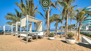 A beachside hotel with white lounge chairs and tables, palm trees, and a clear view of the ocean. - Oceanview 2 BR Condo - Beachclub - Pool - Ocean (Nuevo Nayarit)