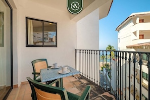 A balcony with a table and chairs, a window, and a view of a building and palm trees.