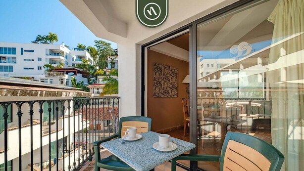 A balcony with a table and chairs, a view of the city, and a door leading to an interior space. - Amazing 2 BR Condo - Partial Oceanview - Pool (Puerto Vallarta)