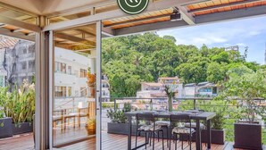 Une terrasse extérieure moderne, dotée d’une porte vitrée donnant sur un patio, d’un plancher en bois et d’une table à manger avec des chaises.