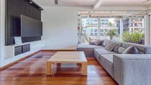 Un salon moderne avec une table basse en bois, un canapé gris et un téléviseur à écran plat fixé au mur.