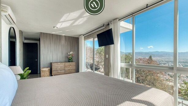 Un dormitorio con una cama grande, un aparador, un televisor y vistas a la ciudad y a las montañas.
