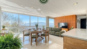 Una sala de estar moderna con comedor, ventanas grandes, un televisor de pantalla plana y una isla de cocina.