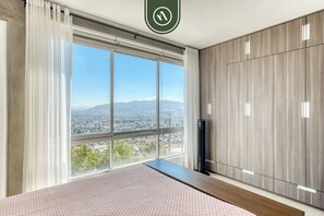 Un dormitorio con un ventanal grande, una cama, un armario y un termostato.