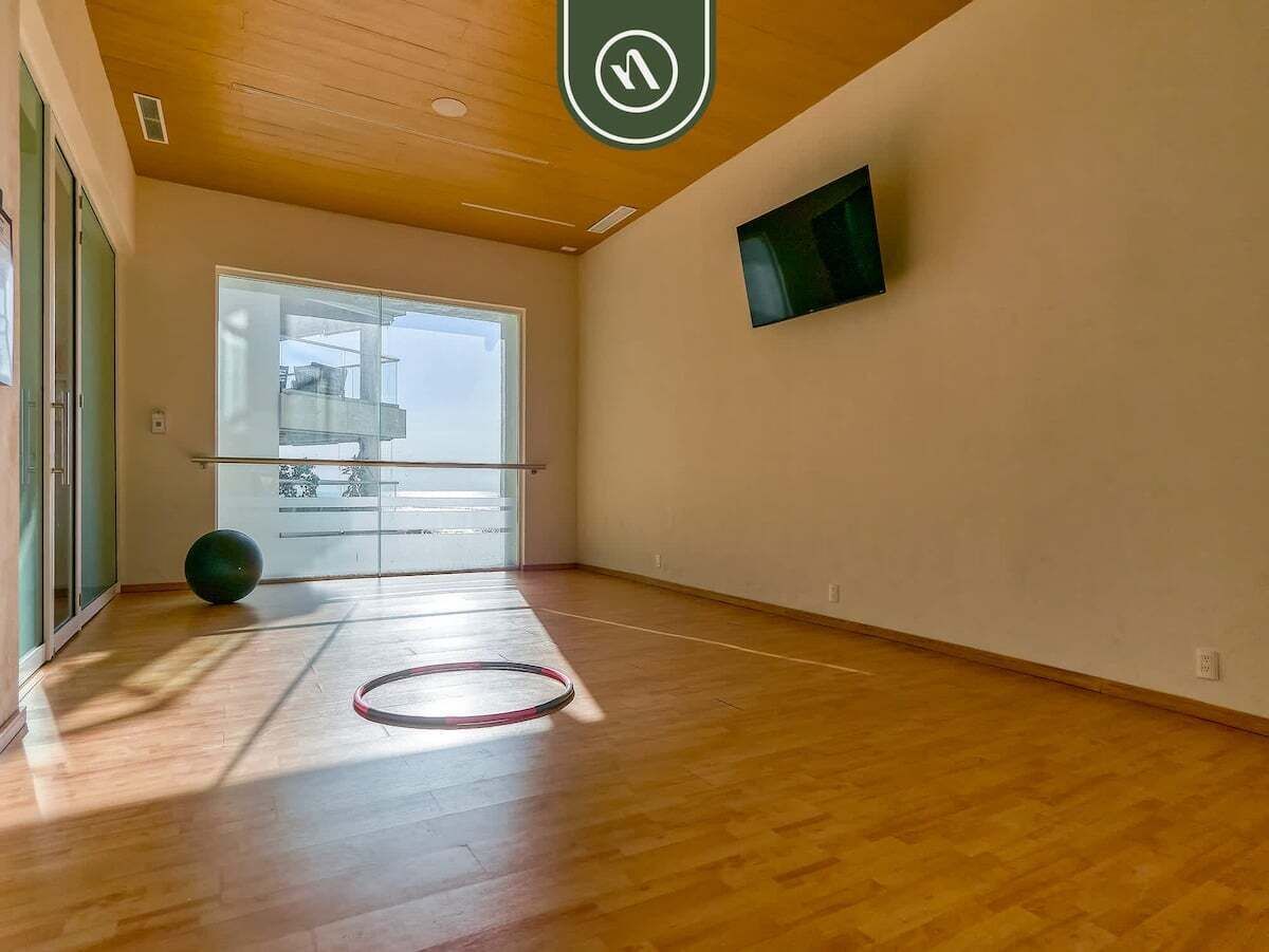 A spacious room with wooden flooring, a large window, and a television mounted on the wall.