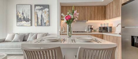 Una cocina moderna con armarios de madera, una isla central con asientos y un comedor con una mesa y sillas blancas.