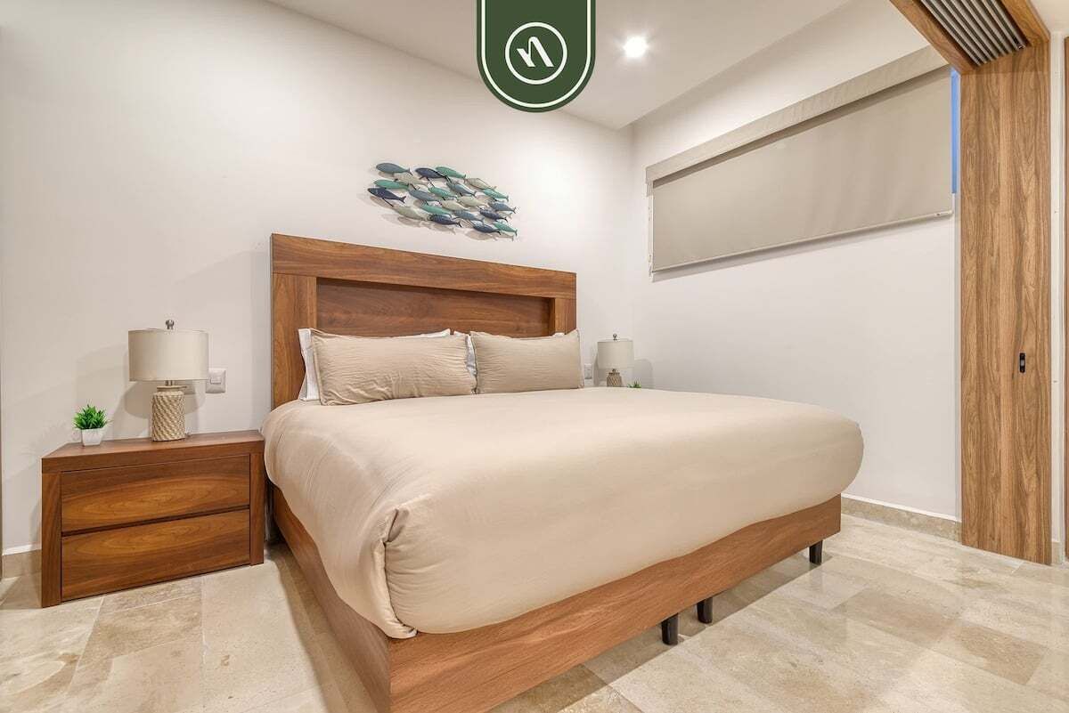 A bedroom with a wooden bed, two bedside tables, a wall-mounted fish decoration, and a large window.