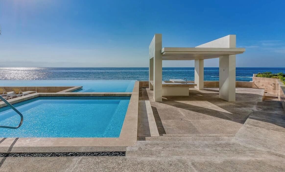 A pool area with a view of the ocean, a covered seating area, and a poolside lounge.