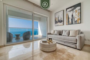 A modern living room with a sofa, a coffee table, and a view of the ocean through large glass doors.
