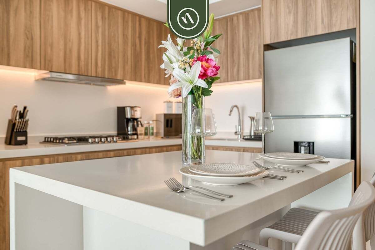 A modern kitchen with a white countertop, a vase with flowers, and a stainless steel refrigerator.