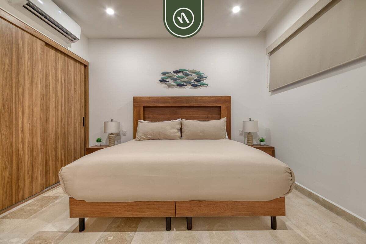 Een slaapkamer met een houten bed, twee nachtkastjes met lampen, een houten garderobe en een kunstwerk aan de wand.