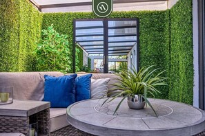 Un espace extérieur moderne, aménagé avec un banc rembourré, une table ronde et un pot de fleurs.