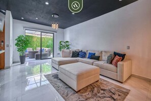 A modern living room with a sectional sofa, a matching ottoman, a large window, and a potted plant.