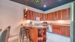 A modern kitchen with wooden cabinets, a central island with stools, and a built-in microwave. - Modern 2BR Condo in Old Town - Private Terrace (Puerto Vallarta)