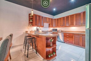 A modern kitchen with wooden cabinets, a central island with stools, a microwave, and a sink.