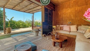 A modern living room with a sofa, coffee table, and TV, overlooking a pool and greenery. - Stunning Two-bedroom Ocean View House - Mazul (Santa María Tonameca)