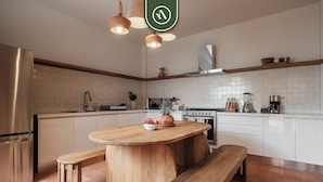 A modern kitchen with a central island, wooden benches, a stainless steel refrigerator, and a hanging light fixture. - Centric 3BR Condo in Downtown in Oaxaca (Oaxaca)