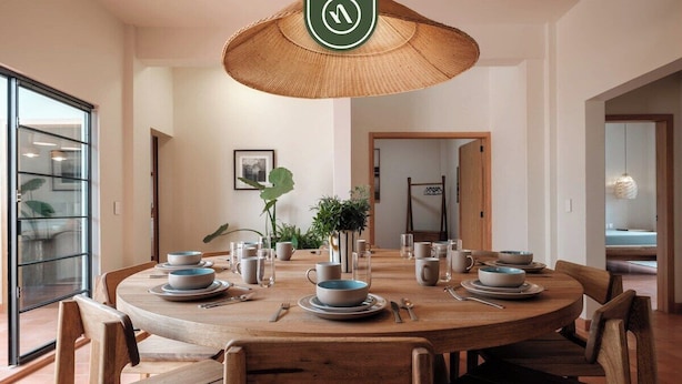 A round wooden dining table with plates, cups, and cutlery, surrounded by wooden chairs. - Centric 3BR Condo in Downtown in Oaxaca (Oaxaca)