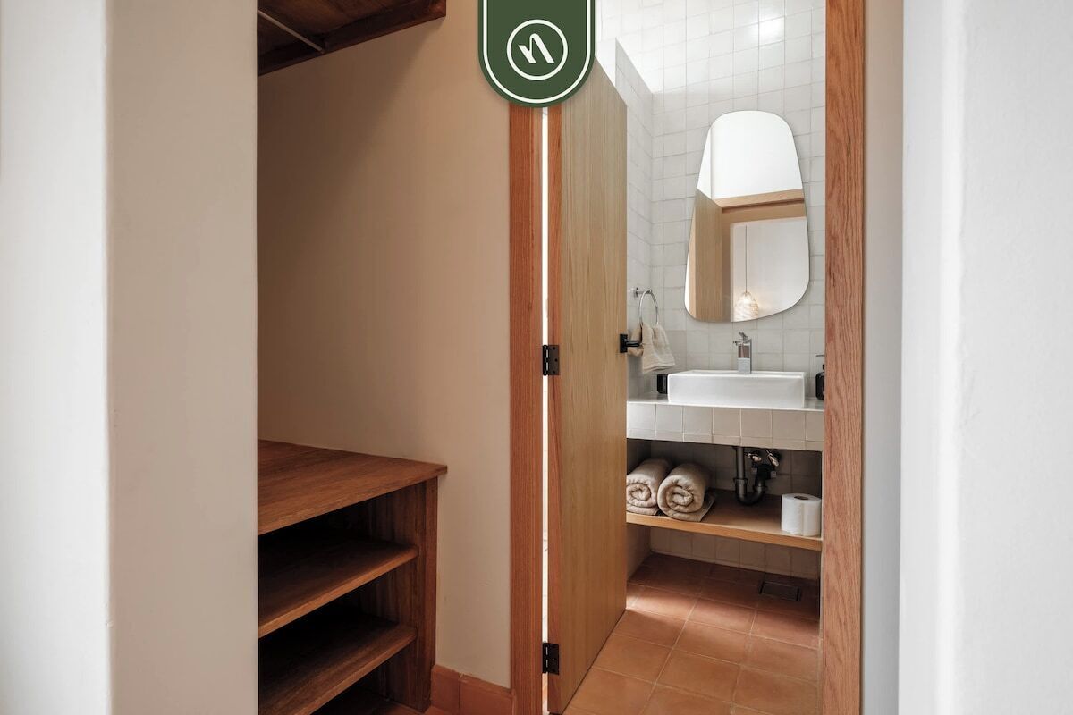 A narrow hallway leading to a bathroom with a wooden door, a white sink, and a mirror.