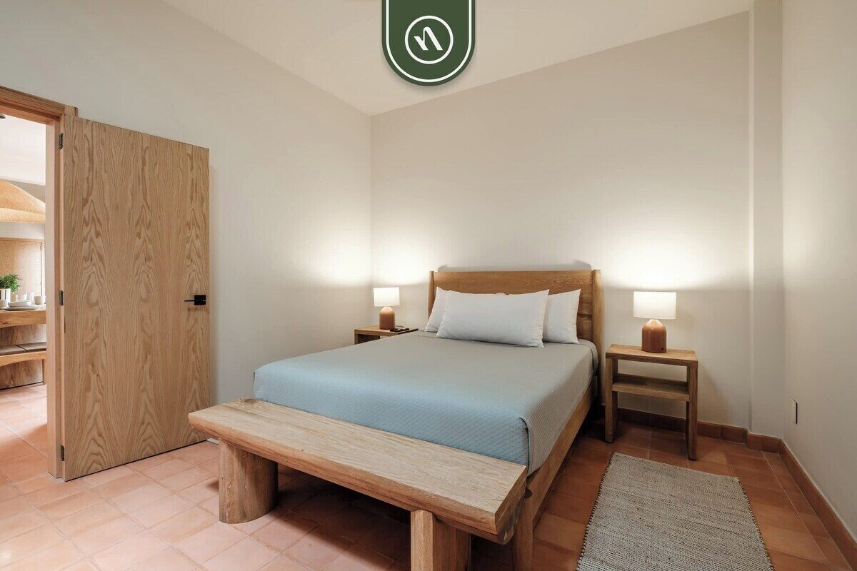 Une chambre à coucher avec un lit, des tables de chevet, un banc et une porte.
