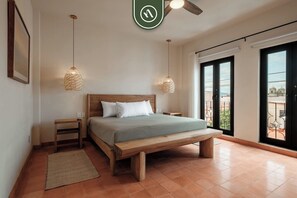 A bedroom with a wooden bed, two bedside tables, a woven pendant light, a large window, and a view of the outside. - Centric 3BR Condo in Downtown in Oaxaca (Oaxaca)