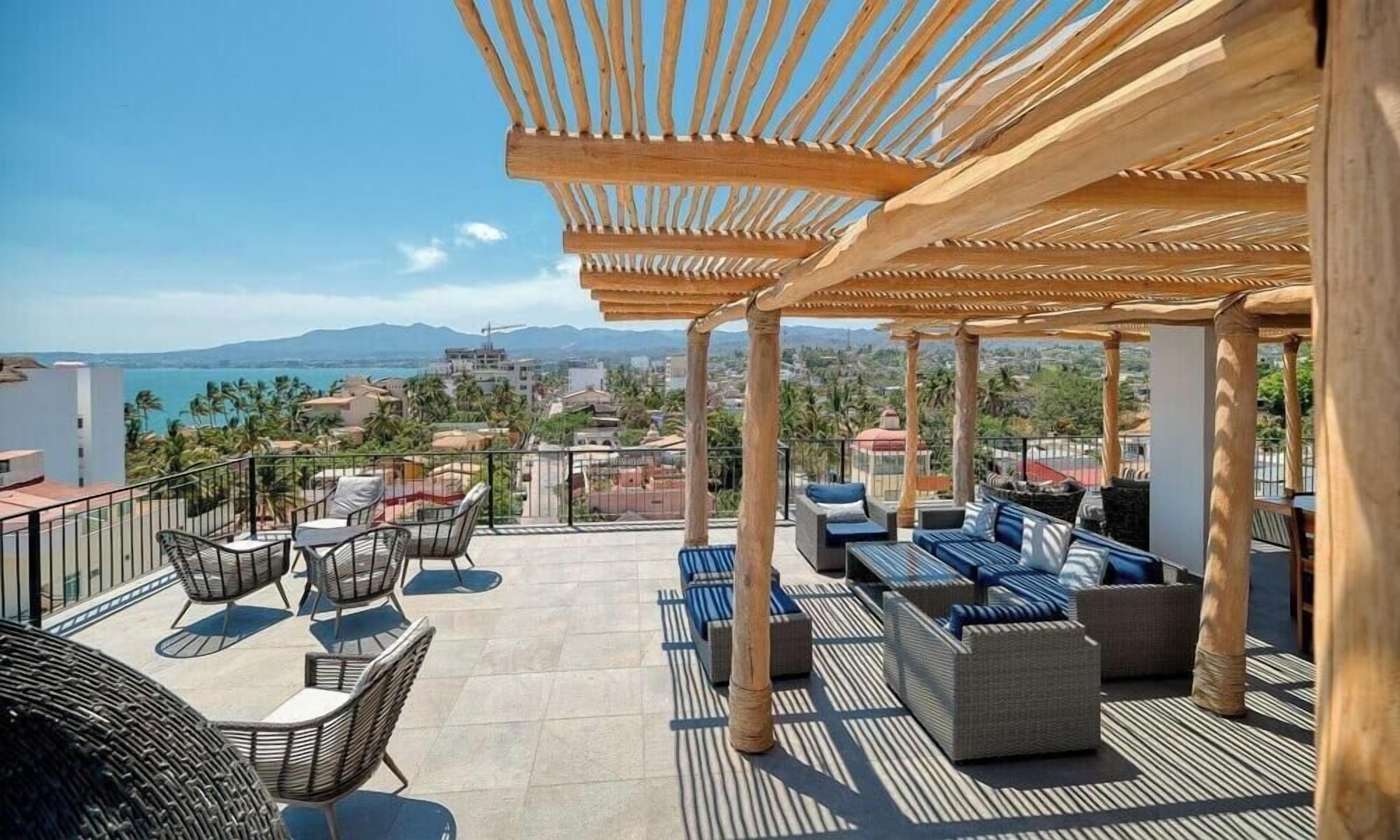 A rooftop terrace with outdoor seating, a pergola, and a view of the city and mountains.