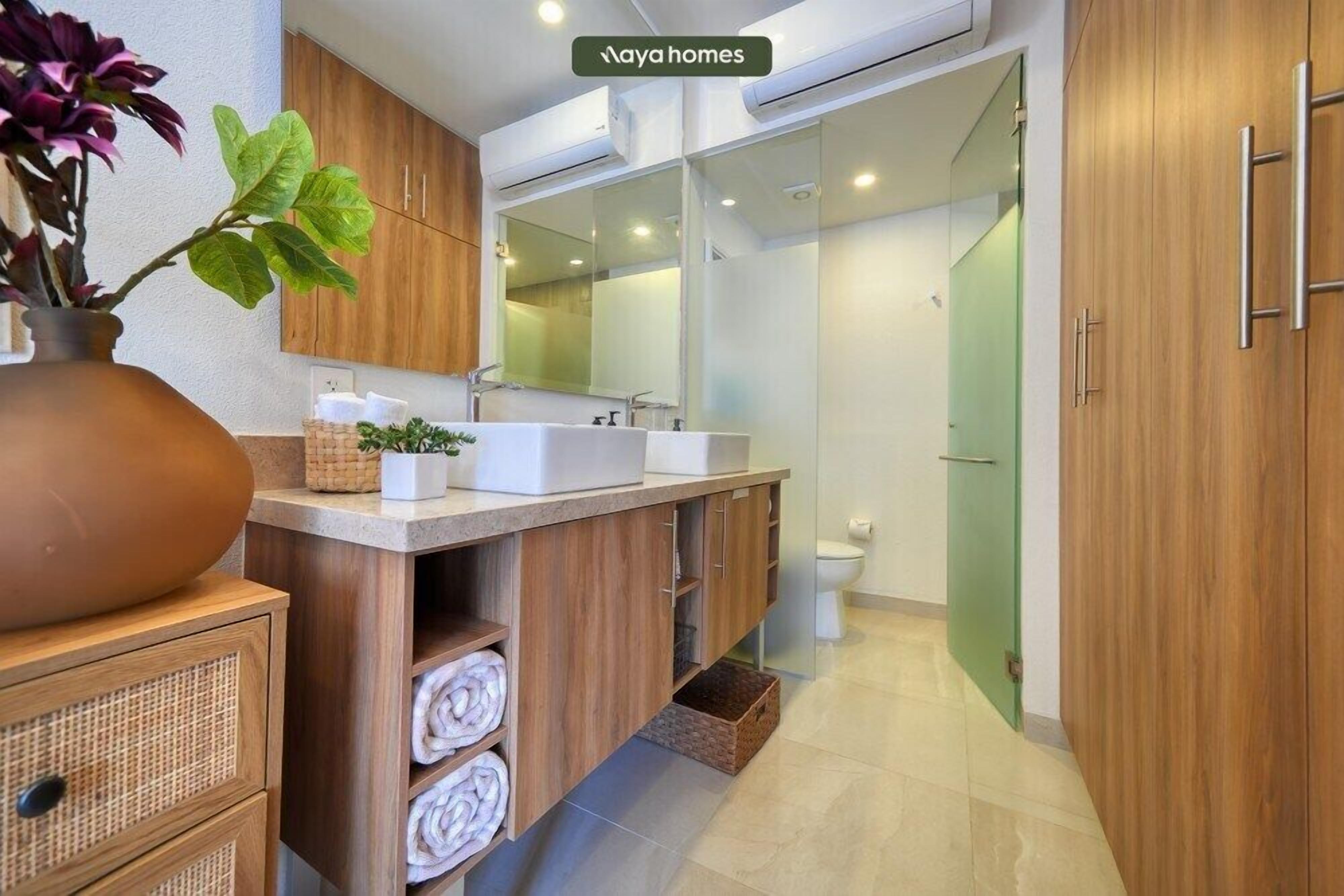 A modern bathroom with wooden cabinetry, a large mirror, and a dual sink vanity.