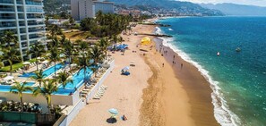 A beach resort with a swimming pool, sun loungers, and a view of the ocean.