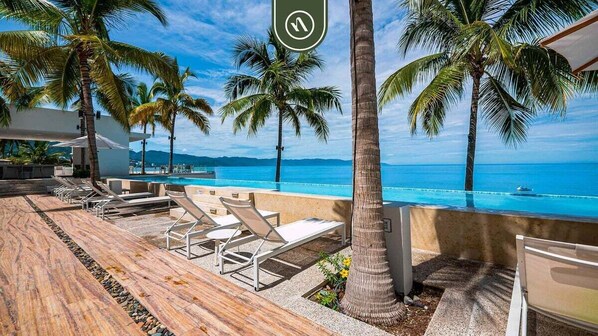A poolside area with lounge chairs, palm trees, and a view of the ocean.